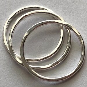 May include: Three silver rings stacked on top of each other. The rings are all smooth and have a hammered texture.
