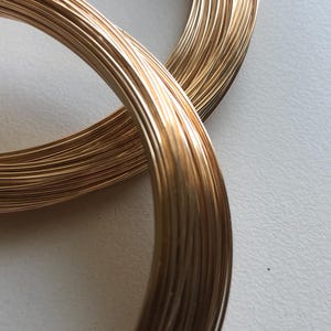 Puede incluir: Primer plano de dos carretes de alambre de color dorado. El alambre está enrollado firmemente alrededor de cada carrete, creando una superficie lisa y brillante.