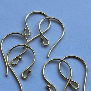 May include: Four gold-toned earring hooks, also known as ear wires, are arranged on a light blue surface. The hooks are made of metal and have a smooth, polished finish.