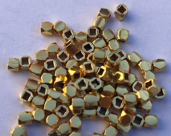 Puede incluir: Un montón de cuentas de metal de color dorado con un agujero cuadrado en el centro de cada cuenta.