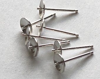 May include: A close-up of six silver earring posts with flat backs. The posts are arranged in a pile on a white surface.