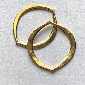 May include: Two gold-toned hammered metal rings, one slightly larger than the other, are stacked on top of each other. The rings are both open and have a slightly irregular shape.
