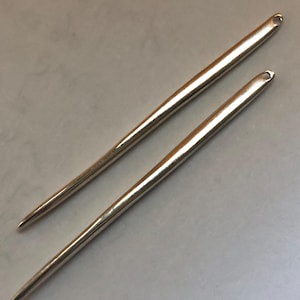 May include: Two silver crochet hooks, one slightly longer than the other, with pointed tips and loop ends.