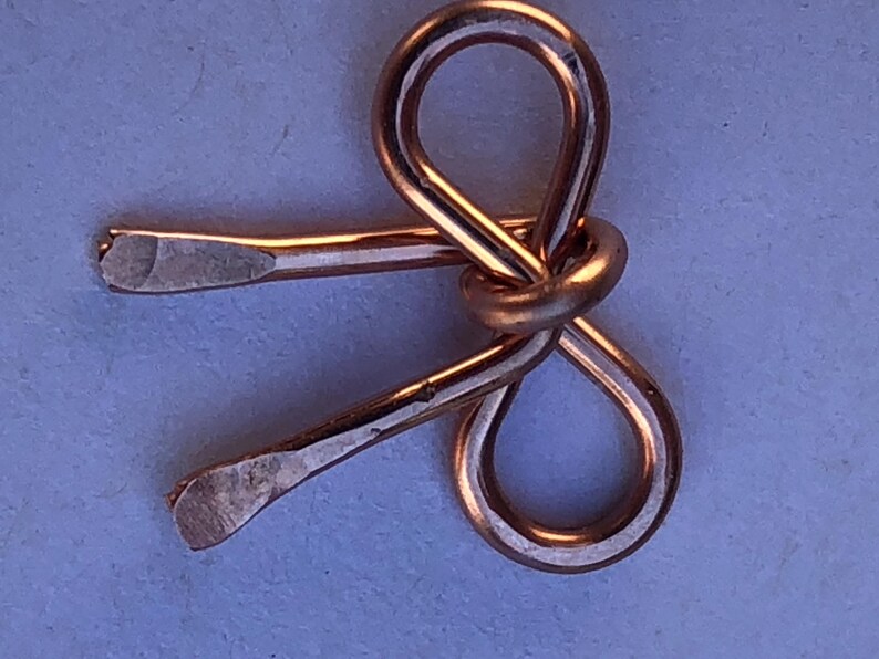 May include: A copper-colored metal bow tie, crafted from a single piece of wire, with a smooth, polished finish.