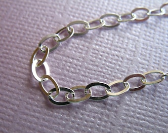 May include: A silver chain necklace with oval links. The chain is on a purple textured background.