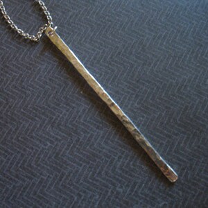 May include: A silver necklace with a long, hammered bar pendant.