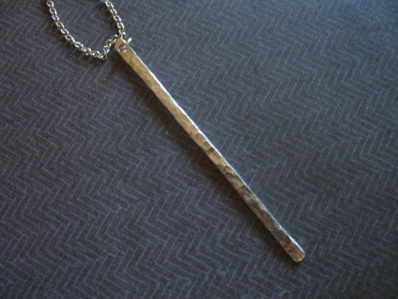 May include: A silver necklace with a long, hammered bar pendant.