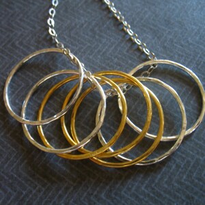 May include: A silver chain necklace with five interconnected rings, three silver and two gold.