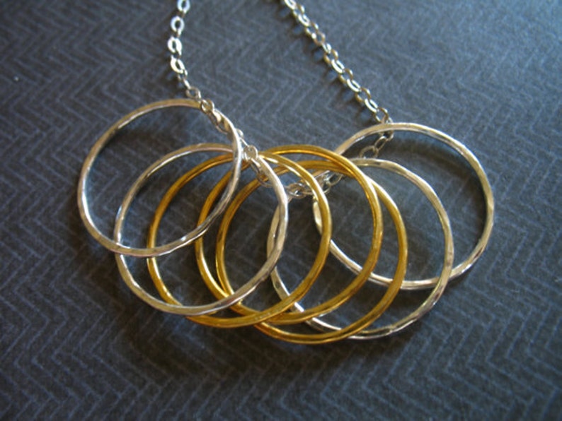 May include: A silver chain necklace with five interconnected rings, three silver and two gold.
