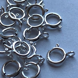 Puede incluir: Un montón de anillos de salto de color plateado con un cierre. Los anillos de salto tienen un diámetro de aproximadamente 1,25 cm.