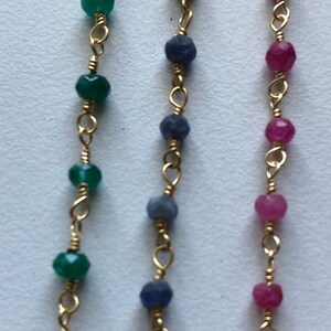 May include: Three gold chains with different colored beads. The chain on the left has green beads, the middle chain has blue beads, and the chain on the right has pink beads.