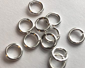 May include: A group of silver jump rings, a type of jewelry finding, scattered on a white surface.