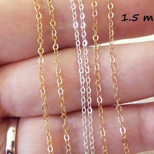 Puede incluir: Se muestran cuatro hebras de cadena, dos doradas y dos plateadas, contra una mano. Las cadenas tienen 1,5 mm de grosor.