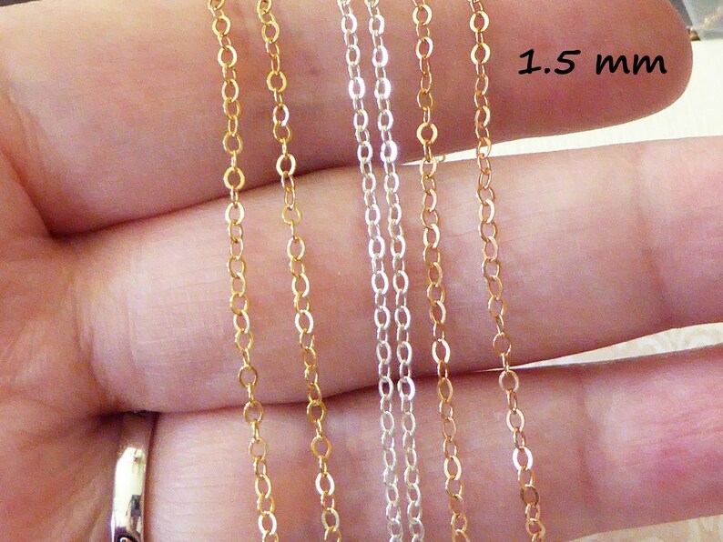 Puede incluir: Se muestran cuatro hebras de cadena, dos doradas y dos plateadas, contra una mano. Las cadenas tienen 1,5 mm de grosor.