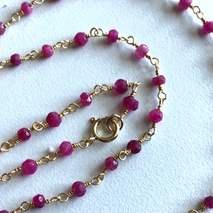 May include: A delicate gold chain necklace with small, faceted pink gemstones. The necklace has a lobster clasp closure.
