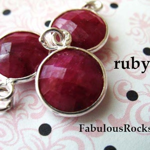 May include: Three ruby red faceted gemstone beads with silver connectors. The beads are connected to form a pendant or charm. The word "ruby" is written in white text on a pink and white background.