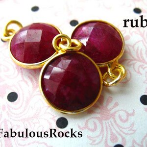 May include: Three ruby red gemstone beads with gold accents. The beads are faceted and have a shiny finish. The word "ruby" is written in black text above the beads.