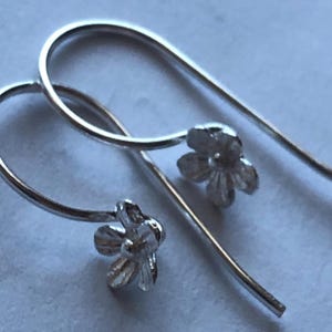 May include: A pair of silver flower dangle earrings. The earrings are made of thin silver wire and feature a small flower charm at the end.