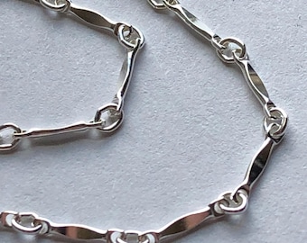Puede incluir: Un collar de cadena de plata con un diseño delicado, plano y ligeramente curvado.