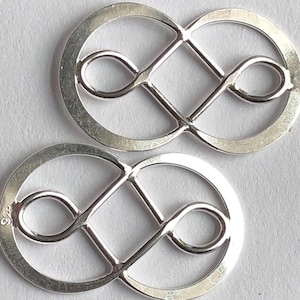 May include: Two silver infinity symbol charms with a decorative knot design. The charms are made of metal and have a shiny finish.