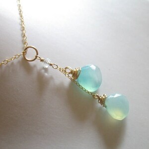 Puede incluir: Un delicado collar de cadena dorada con dos colgantes de piedra preciosa azul claro. El collar presenta un peque&ntilde;o dije circular y un solo cristal transparente.