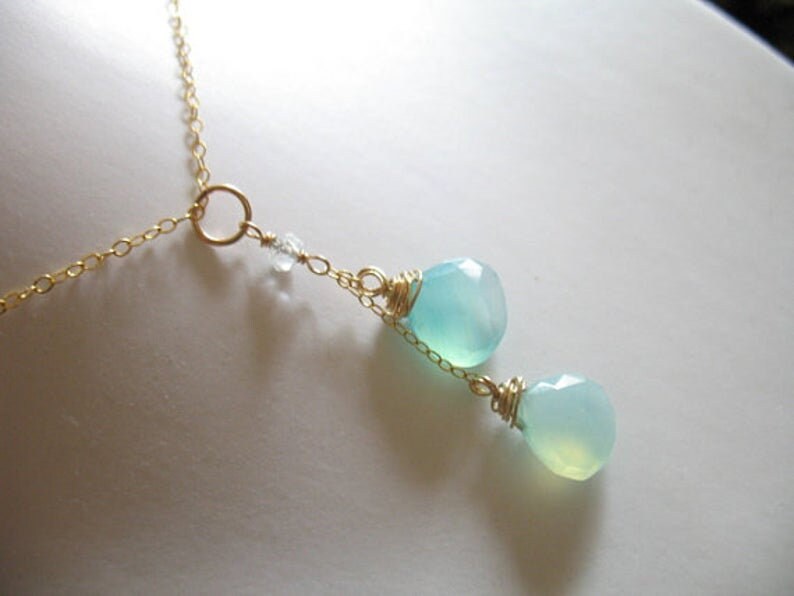 Puede incluir: Un delicado collar de cadena dorada con dos colgantes de piedra preciosa azul claro. El collar presenta un peque&ntilde;o dije circular y un solo cristal transparente.