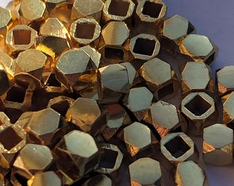May include: A pile of gold-colored metal beads with a square hole in the center of each bead. The beads are faceted and have a shiny finish.