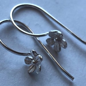 May include: A pair of silver dangle earrings with a small flower design at the end of each earring.