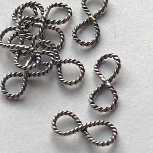 May include: A pile of silver-toned infinity symbol charms with a twisted rope design.