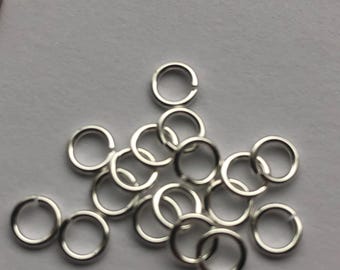 May include: A pile of silver jump rings, a type of jewelry finding used for connecting chains, cords, and other jewelry components.