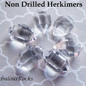 May include: Six clear, undrilled Herkimer diamonds on a white background. The diamonds are all double-terminated and have a natural, rough finish. The text "Non Drilled Herkimers" and "FabulousRocks" is visible in the image.