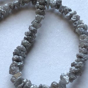 May include: A strand of rough, gray diamonds strung together as a necklace. The diamonds are irregular in shape and have a matte finish.
