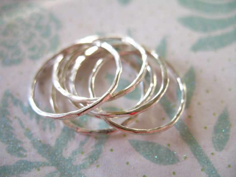 May include: A set of six silver rings, each with a hammered texture, stacked on top of each other.