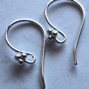 May include: A pair of silver hoop earrings with a cluster of three small silver beads on each hoop.