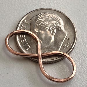 Może przedstawiać: Miedziany symbol nieskończoności, spoczywający na srebrnej monecie. Moneta przedstawia profil osoby i rok 2021. Symbol nieskończoności wykonany jest z cienkiego, zaokrąglonego metalu.