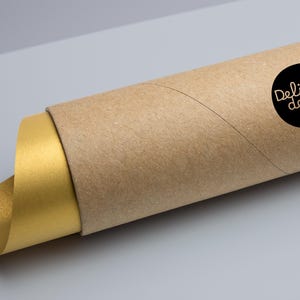 Puede incluir: Un p&oacute;ster o impresi&oacute;n enrollada, con una superficie dorada visible en el extremo. El p&oacute;ster est&aacute; encerrado en un tubo de cart&oacute;n marr&oacute;n. Una pegatina circular negra con el texto "Delish decore." est&aacute; en el tubo.