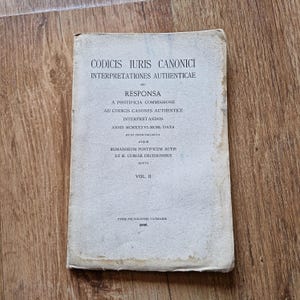 May include: A vintage book titled "CODICIS IURIS CANONICI INTERPRETATIONES AUTHENTICAE" with text in Latin. The cover is off-white with black text and shows signs of wear. The book is volume II and was printed by Typis Polyglottis Vaticanis.