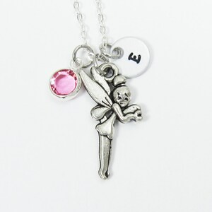 Puede incluir: Collar de plata con un dije de cristal rosa, un dije de Campanilla y un dije de plata con la letra E.