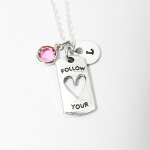 Puede incluir: Collar de plata con un dije de cristal rosa, un dije de plata con la palabra "FOLLOW" y un corazón recortado, y un dije de plata con la letra "I". El collar dice "FOLLOW YOUR" en el dije.