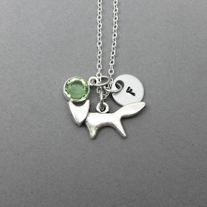 Könnte beinhalten: Silberne Halskette mit einem Fuchs-Anhänger, einem grünen Edelstein und einer silbernen Scheibe mit dem Buchstaben "F" darauf.