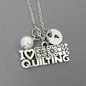 Puede incluir: Collar de plata con un dije que dice "Me encanta acolchar" con un corazón y diseños de bloques de acolchado. El collar también tiene una perla y un pequeño dije redondo con la letra "P" en él.