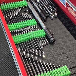 May include: A red metal tool chest drawer containing a large collection of chrome wrenches organized in rows. Each wrench features a bright green plastic handle grip labeled with its specific size. A long torque wrench lies horizontally at the top.
