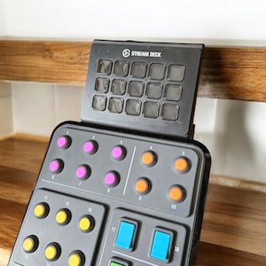 May include: A black Stream Deck with 20 buttons. The top row of buttons are grey and the bottom three rows have different coloured buttons. The buttons are numbered 1 through 20.