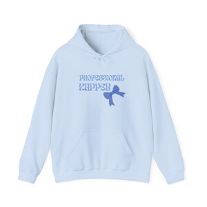 Puede incluir: Una sudadera con capucha azul claro con un lazo azul y el texto "PROFESSIONAL ZAPPER" en una fuente retro.