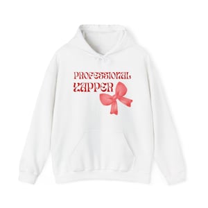 Puede incluir: Sudadera con capucha blanca con el texto "PROFESSIONAL ZAPPER" en letras rojas y un gráfico de lazo rosa.