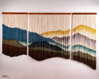 May include: A wall hanging made of yarn with a landscape design. The hanging is divided into three sections, each with a different colour scheme. The left section is blue, green, and brown. The middle section is blue, green, and yellow. The right section is purple, green, and yellow.
