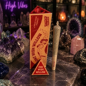 Puede incluir: Una caja de cartón triangular etiquetada como One Wish Willow con gráficos en rojo y beige, que incluye el texto Amaze your friends y You only get one wish. Junto a ella hay un cono de papel preenrollado con un filtro marcado como RAW.