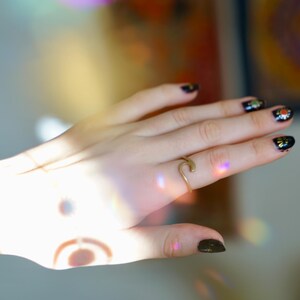 May include: A hand with black nail polish with gold glitter accents, wearing a gold wave ring.