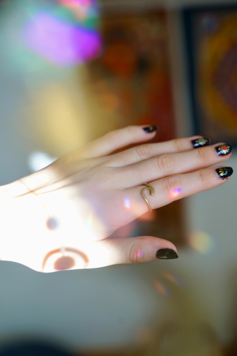 May include: A hand with black nail polish with gold glitter accents, wearing a gold wave ring.