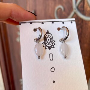 May include: A pair of silver hoop earrings with a white oval-shaped stone hanging from each hoop.